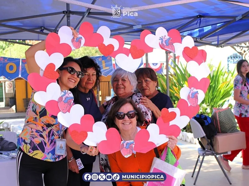 Vecinas sonríen dentro de un marco de corazones en la feria de salud del CESFAM