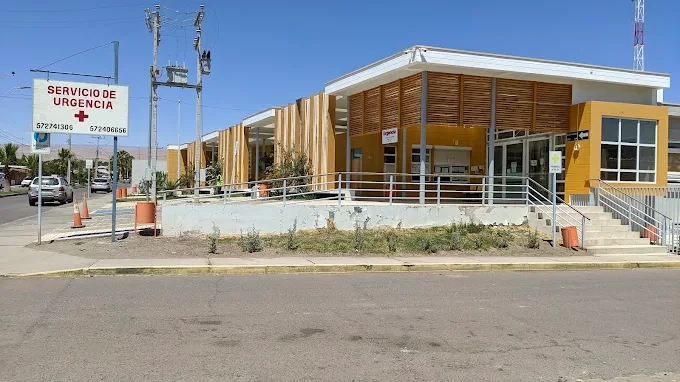 Fachada del CESFAM de Pica, con revestimiento de madera y paredes amarillas, y el letrero del Servicio de Urgencia